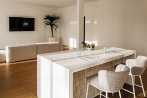 A modern kitchen with a central island, bar stools, a sofa, and a TV mounted on the wall.