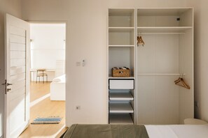 A bedroom with a bed, a wardrobe with shelves, a hanging rack, and a small table with chairs.