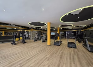 Ein Fitnessstudio mit Laufbändern, Crosstrainern und Holzboden.