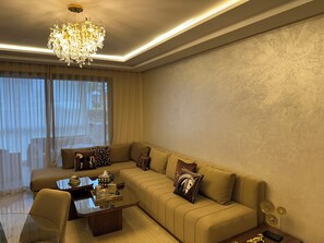 Ein modernes Wohnzimmer mit einem Ecksofa, einem Glastisch und einer Deckenleuchte.