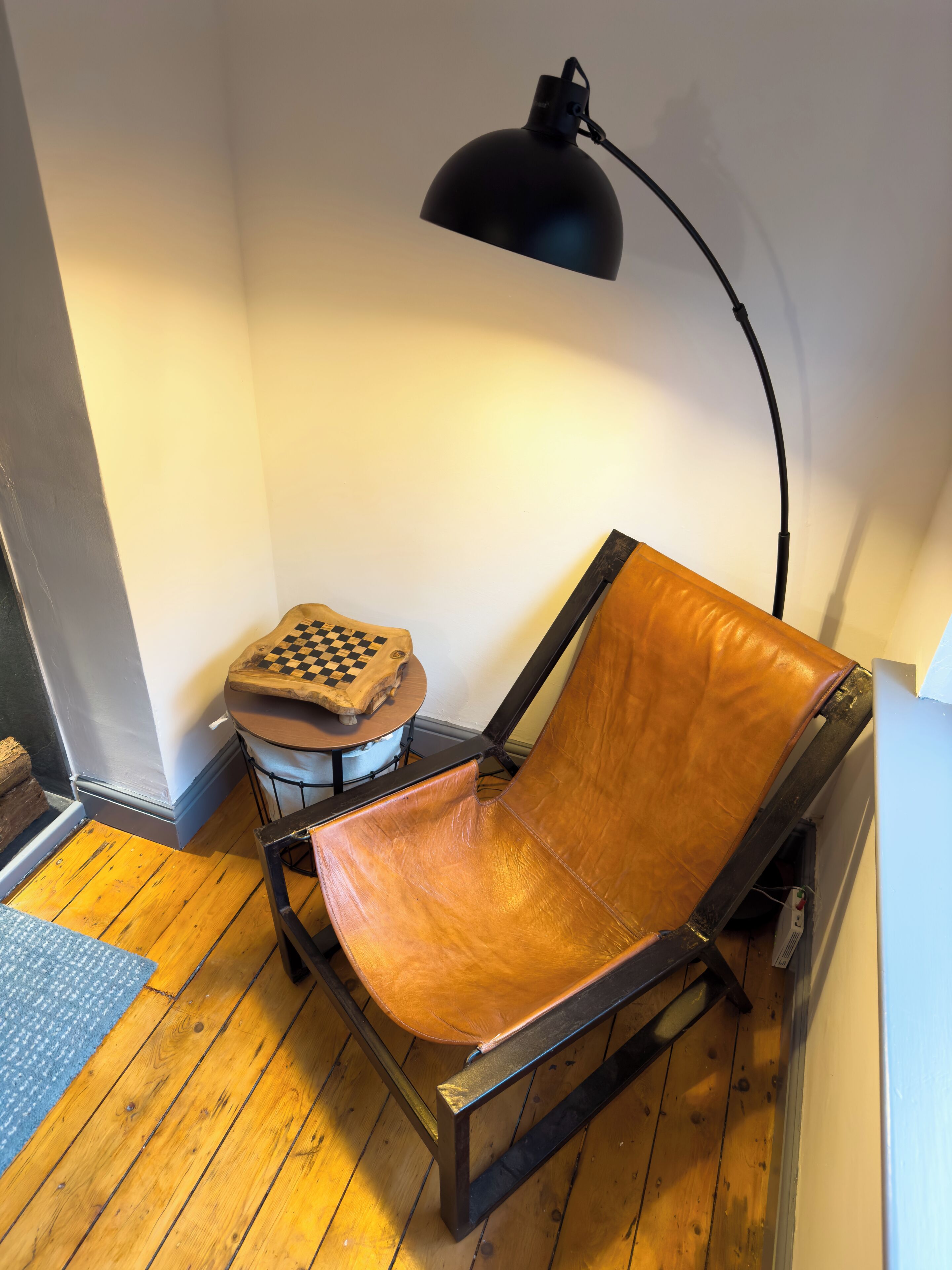 Une chaise avec un siège et un dossier en cuir, une petite table avec un plateau à carreaux et une lampe de bureau noire.