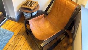 Una silla con asiento y respaldo de cuero, una mesita con cubierta a cuadros y una lámpara de escritorio negra.