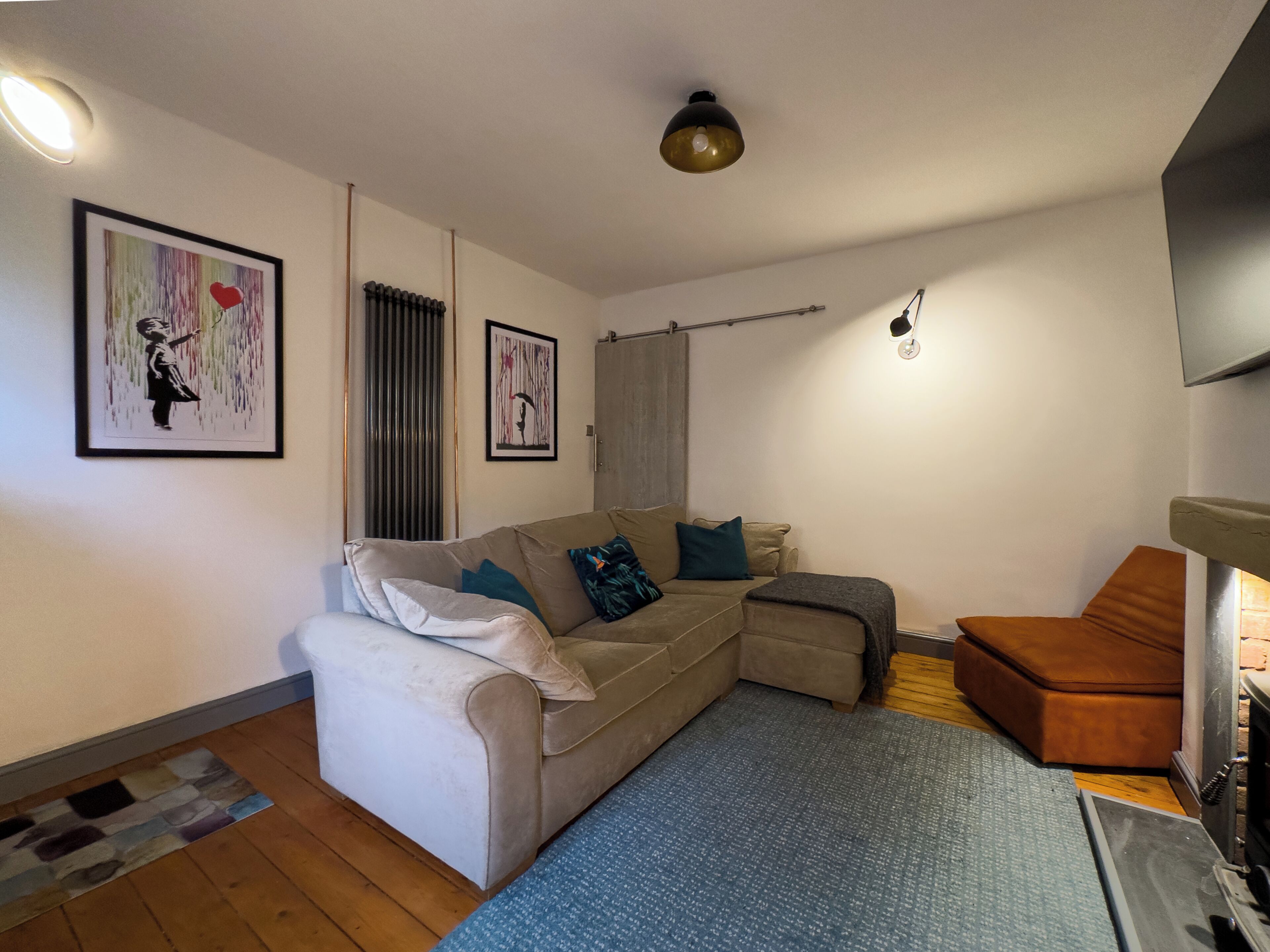 Un salon avec un canapé, un pouf et une cheminée. Deux œuvres d’art encadrées ornent le mur.