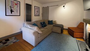 Una sala de estar con un sofá, un reposapiés y una chimenea. Hay dos obras de arte enmarcadas en la pared.