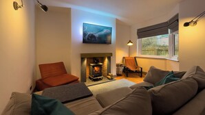 Una sala de estar acogedora con chimenea, un sofá, un sillón y un televisor instalado en la pared.