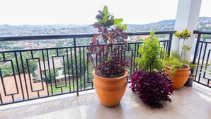 A balcony with potted plants, a tiled floor, and a view of a distant cityscape. - Imaani Living Buziga (Kampala)