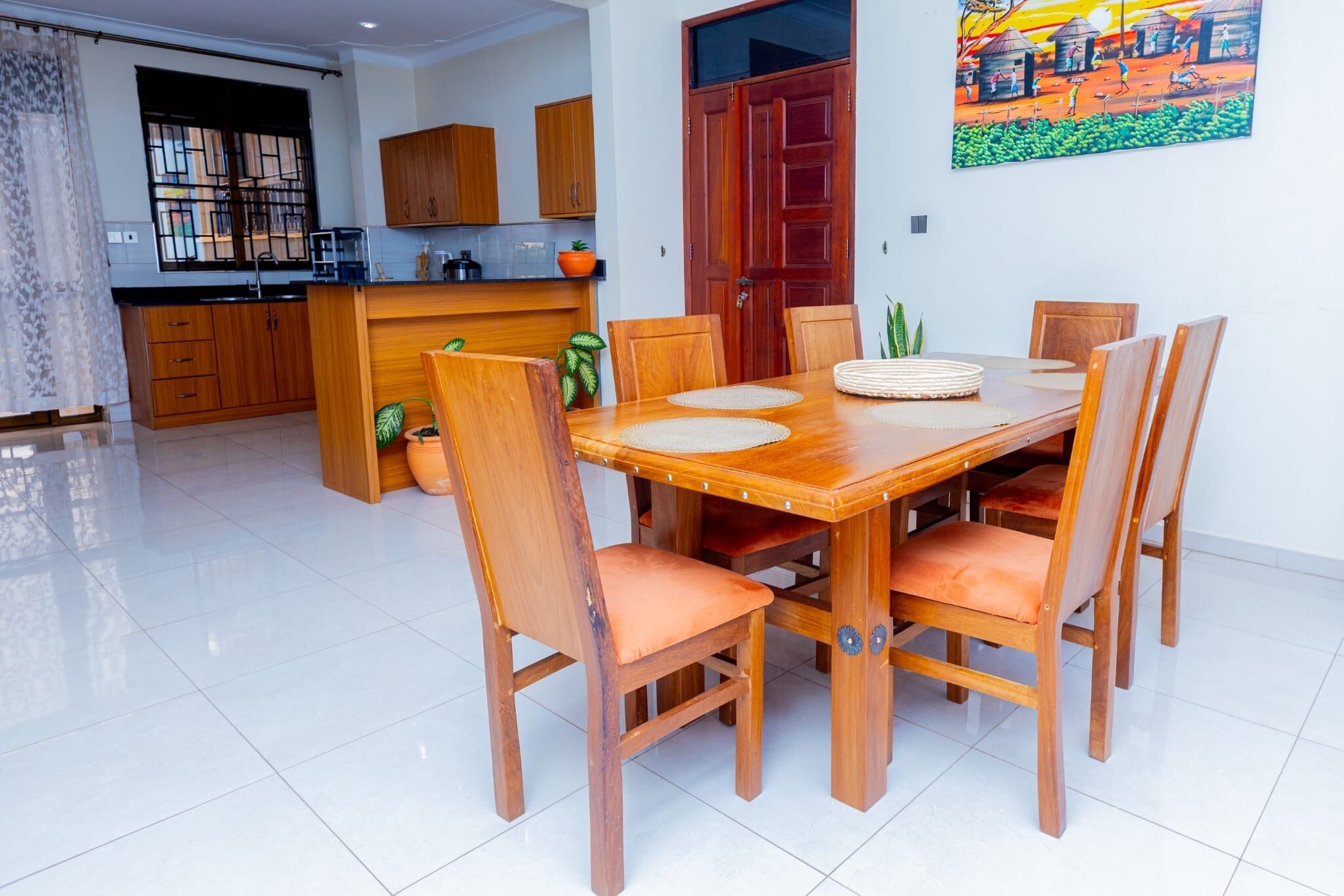 Un comedor con una mesa y sillas de madera, una cocina al fondo y una puerta decorada con un cuadro.
