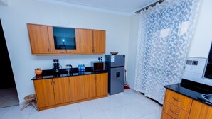 A kitchen with wooden cabinets, a refrigerator, a microwave, and a sink. - Imaani Living Buziga (Kampala)