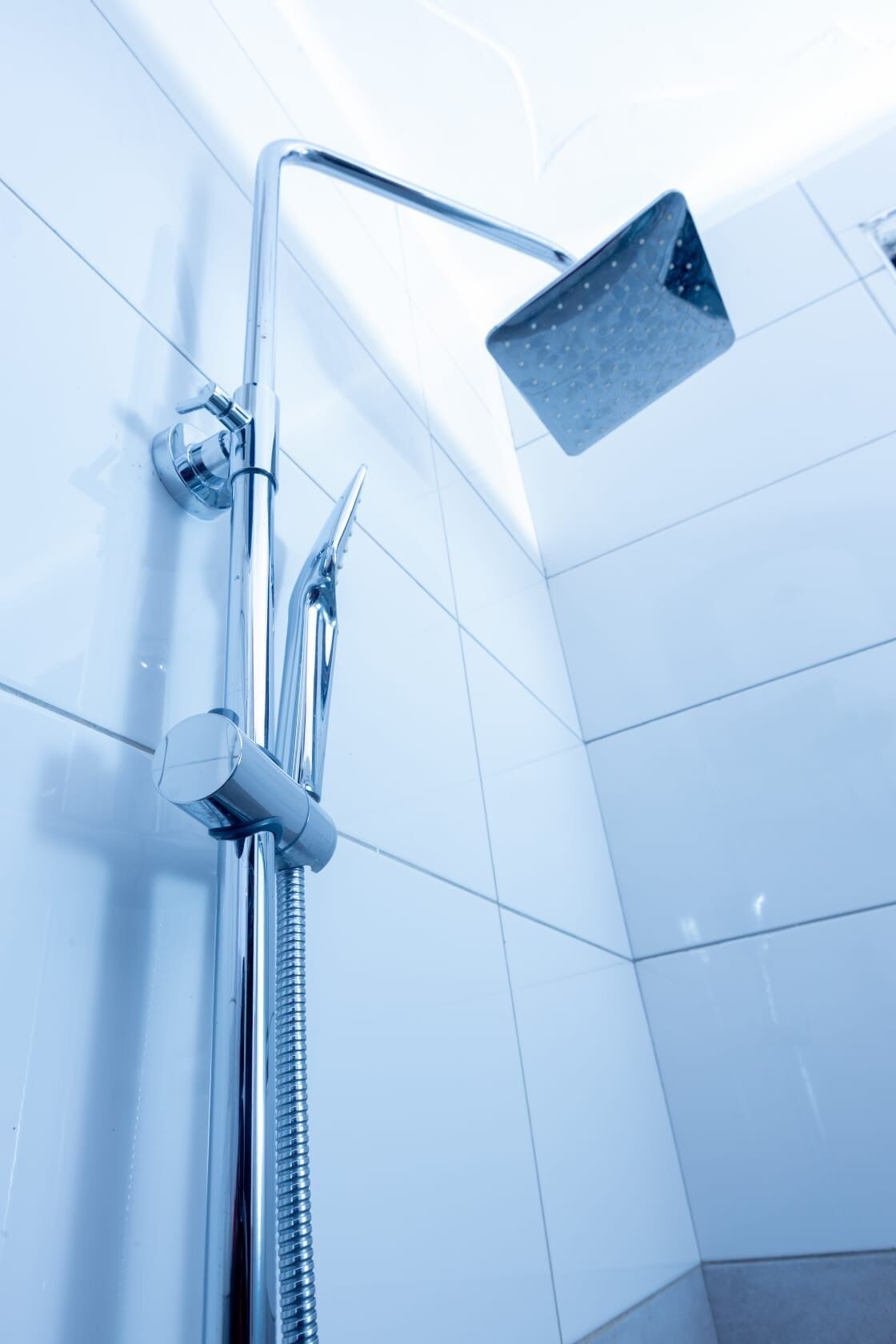 Una ducha con cabezal de ducha de mano y un cabezal de ducha fijo en el techo, en un baño con azulejos.