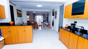 A modern kitchen with wooden cabinets, a dining area with a table and chairs, and a hallway leading to a living space. - Imaani Living Buziga (Kampala)