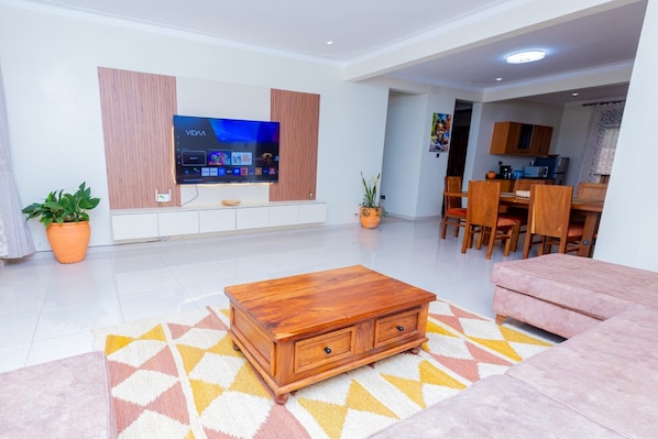 Una sala de estar moderna con un televisor de pantalla plana, muebles de madera, un comedor y una cocina al fondo.