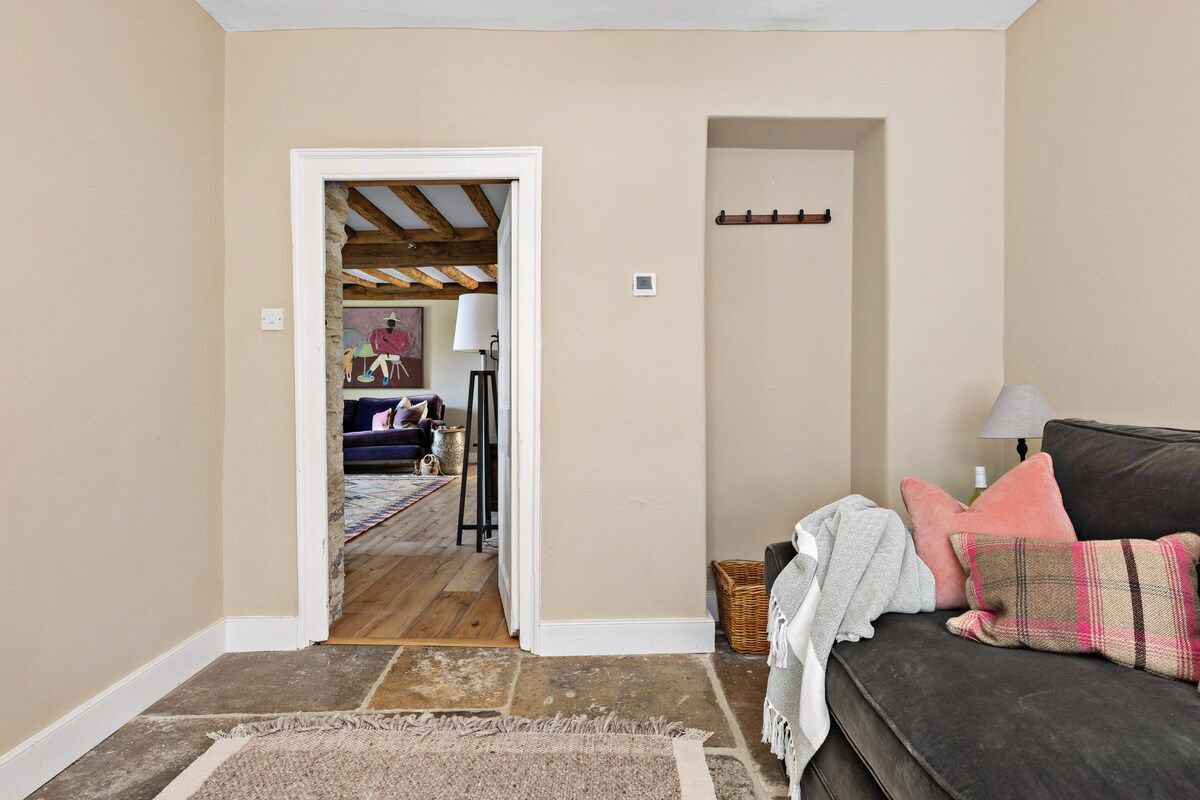A room with a dark-colored sofa, a patterned rug, and a doorway leading to another room with a bed and a lamp.