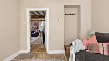 A room with a dark-colored sofa, a patterned rug, and a doorway leading to another room with a bed and a lamp.