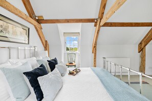 A bedroom with a bed, pillows, a tray with items, a window, a chair, and a radiator.