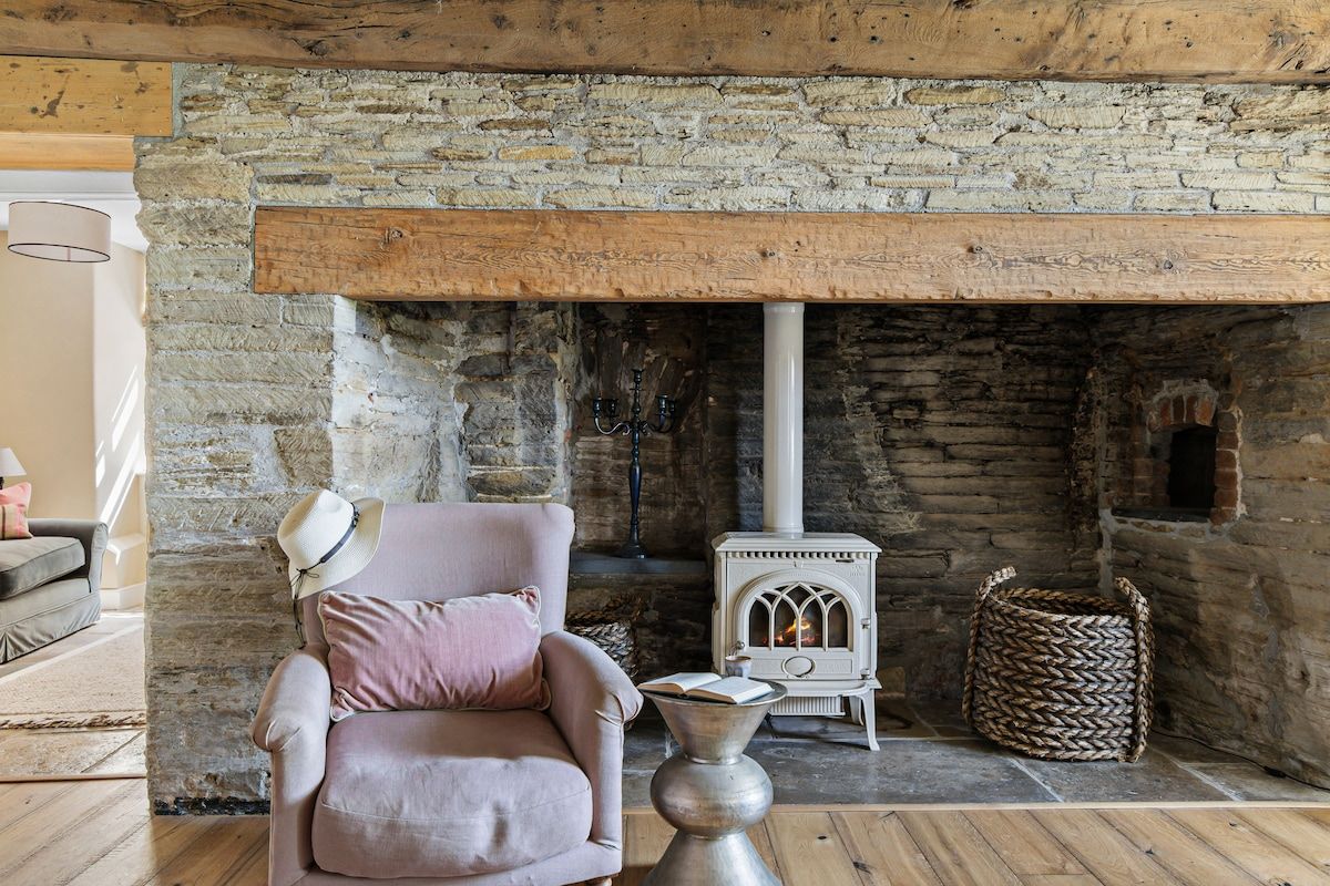 A cozy room with a stone fireplace, a comfortable armchair, and a small white stove.
