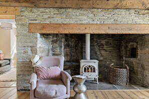 A cozy room with a stone fireplace, a comfortable armchair, and a small white stove.