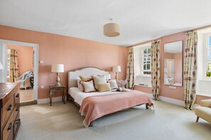 Une chambre à coucher avec un grand lit, deux tables de chevet, une commode, un miroir et une fenêtre avec des rideaux.
