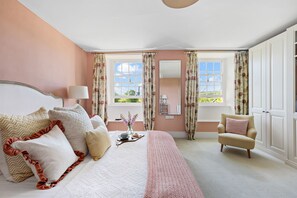 Une chambre à coucher comprenant un lit, une chaise, une fenêtre avec des rideaux, un miroir et une table de chevet avec une lampe.