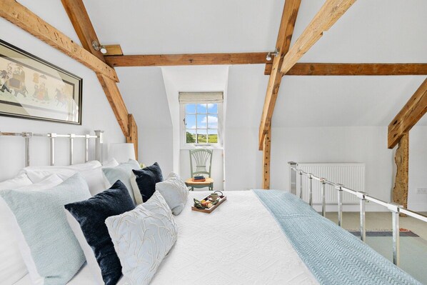 A bedroom with a sloped ceiling, a bed with pillows, a window with a view, and a radiator.