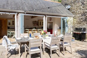 An outdoor dining area with a table set for four, surrounded by wooden chairs.