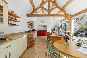 A kitchen with wooden beams, a dining area with a table and chairs, and a view of the outdoors.