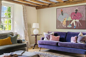 Une pièce avec un canapé violet, un canapé vert, une lampe et un tableau au mur.