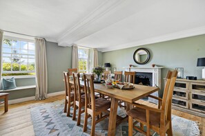 A dining room with a wooden table, chairs, a fireplace, and a view of greenery outside.