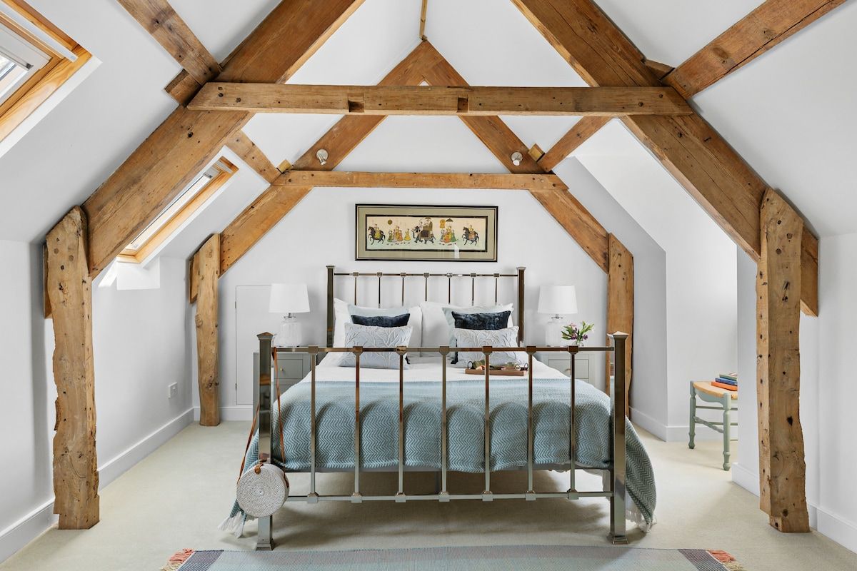 Une chambre avec un plafond en pente, des poutres en bois, un lit avec un cadre en métal et un tableau accroché au mur.