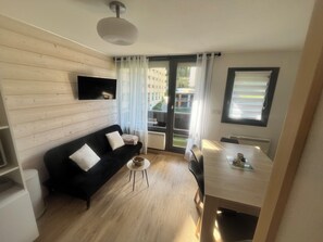 A modern living room with a black sofa, a small round table, and a dining table with chairs. - Les Menuires cosy apartment at the foot of the slopes for a family of 4 people (Les Belleville)