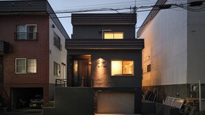A modern two-story building with a garage, a lit entrance, and a visible staircase. - Sauna & Villa Yu to Yo (Chuo-ku, Sapporo City)
