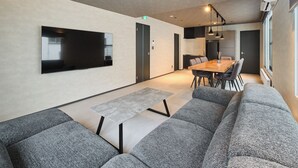 A modern living room with a flat-screen TV, grey sofas, a wooden dining table, and pendant lighting. - Sauna & Villa Yu to Yo (Chuo-ku, Sapporo City)