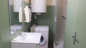 Une petite salle de bain comprenant un lavabo, un lave-linge et une douche.