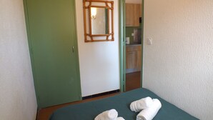 Une pièce avec un lit, une porte verte, un miroir et une vue sur un coin cuisine.