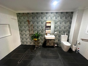 A bathroom with a marble wall, a sink, a toilet, and a potted plant.