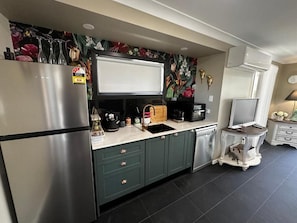 A kitchen with a stainless steel refrigerator, a microwave, a sink, and a dishwasher. There is a decorative wall with floral wallpaper above the counter.