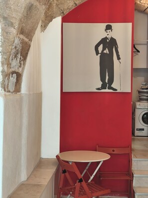 Ein Zimmer mit roter Wand, weißer Decke, einem kleinen Tisch mit Stuhl und einer Waschmaschine.