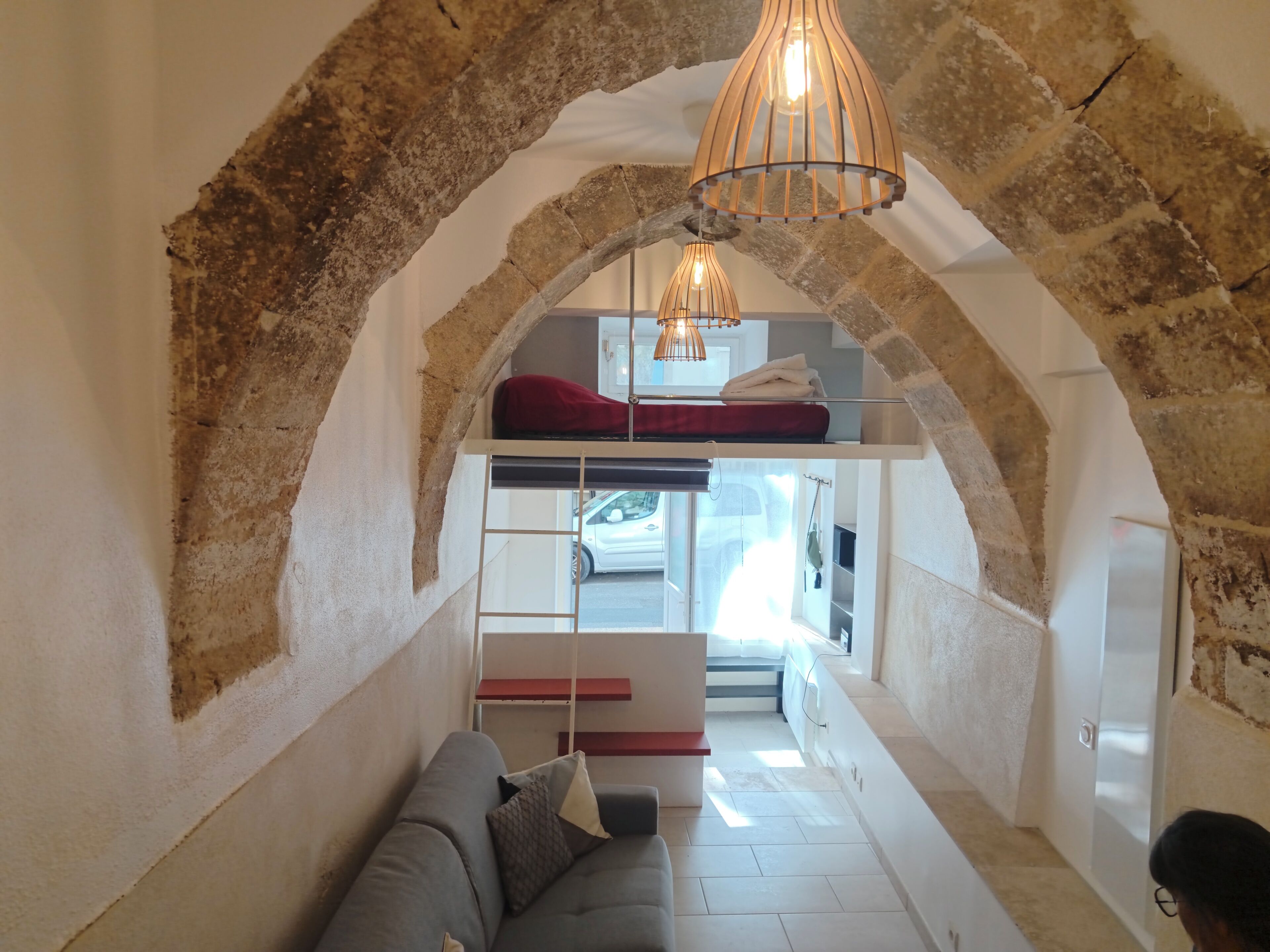 Une pièce chaleureuse avec une arche en pierre, un lit superposé, un canapé et un luminaire suspendu.