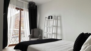 Une chambre à coucher moderne avec un grand lit, une chaise, une échelle et une vue sur l’extérieur à travers des rideaux légers.
