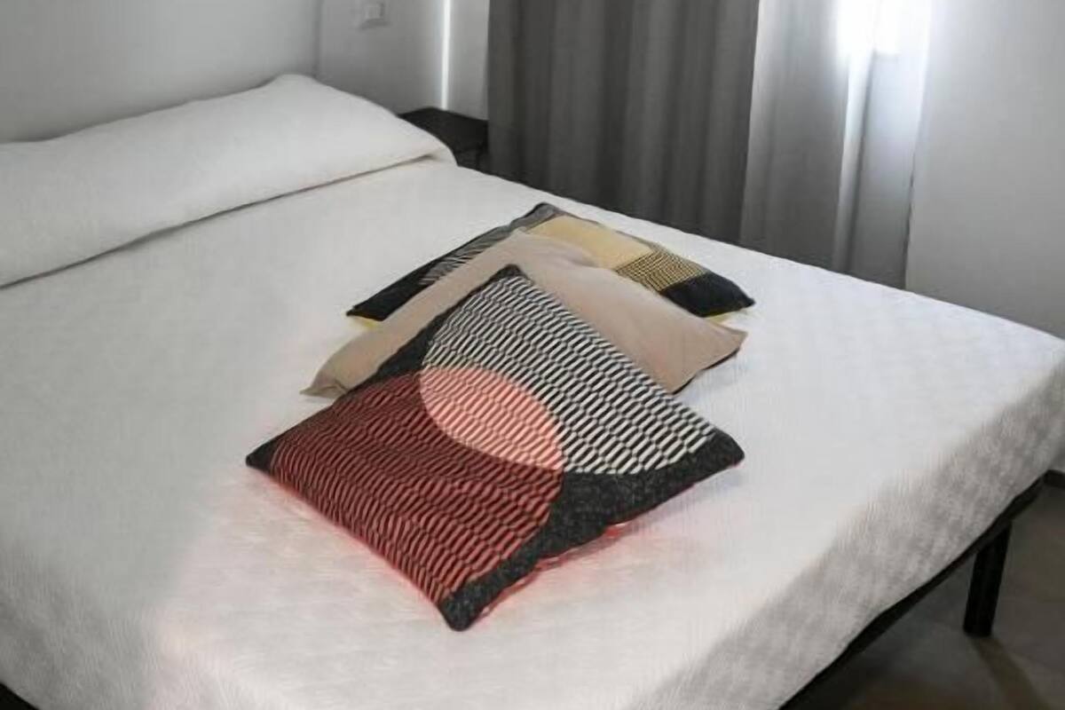 Una cama con sábana blanca, un cojín estampado y una colcha.