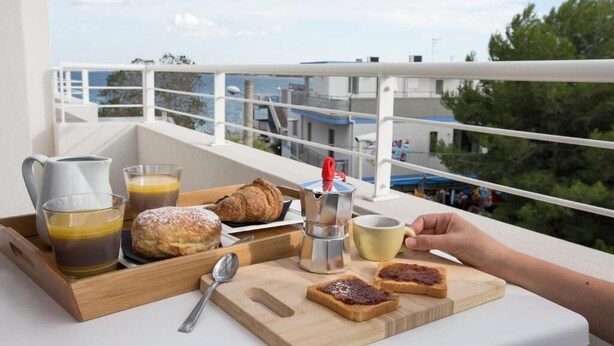 Un vassoio con croissant, pane tostato e caffè su un balcone con vista sulla città.
