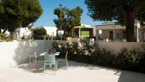 Patio esterno con tavolo e sedie, circondato da alberi e edifici.