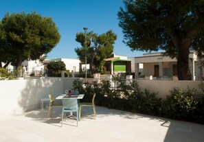Eine Terrasse im Freien mit Tisch und Stühlen, umgeben von Bäumen und Gebäuden.