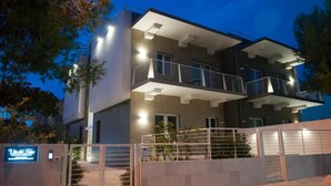 Un edificio moderno su due piani con ingresso chiuso da cancello e un balcone al piano superiore, con un'insegna che indica un'attività commerciale o un servizio.
