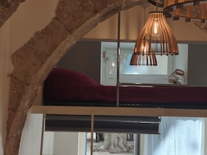 Ein Etagenbett mit rotem Kopfkissen, einer Hängelampe und einem Fenster mit Blick ins Freie.
