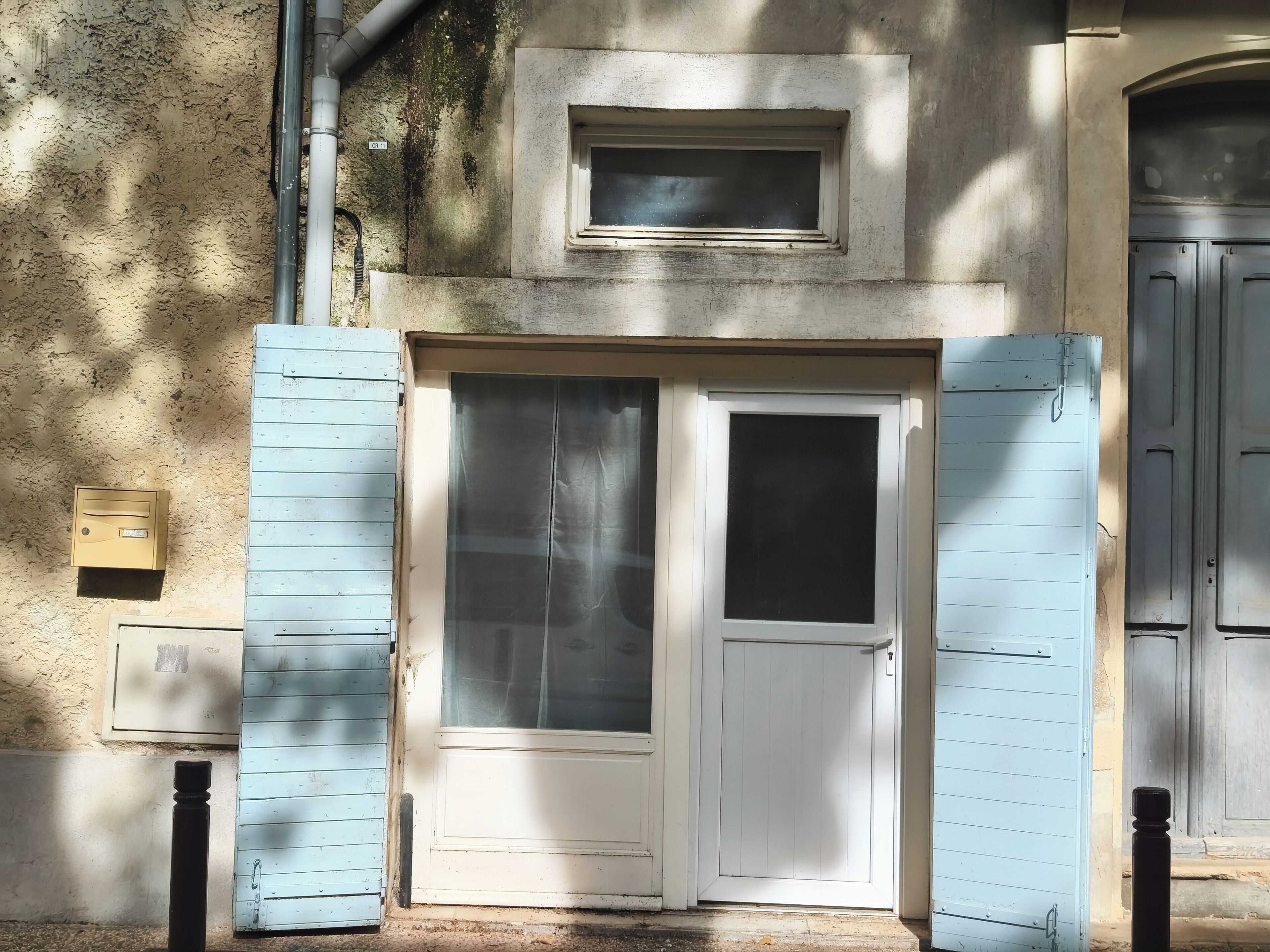 Un edificio con una puerta blanca, un pequeño ventanal encima y una puerta con persiana azul.