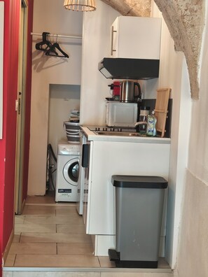 Eine kompakte Küche mit Waschmaschine, einem kleinen Mülleimer und einer Kaffeemaschine.