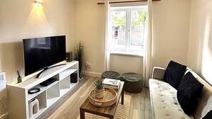 A living room with a flat-screen TV, a sofa, a coffee table, and a window with a view of buildings. - Modern London Stay for 5|Parking| Excel, City Airport & Canary Wharf (London)