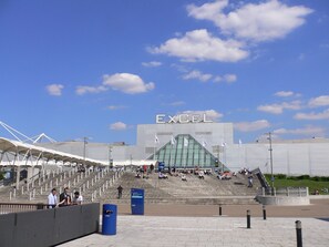 Ein Stadion mit einem großen 'EXCEL'-Schild, Stufen, die zum Eingang führen, und einem klaren Himmel.