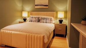 A neatly made bed with a headboard, two bedside tables with lamps, a wall-mounted painting, and a wooden nightstand. - Bankhouse Troon, Scotland | Luxury Sea View Retreat with Hot Tub & Sauna (Troon)