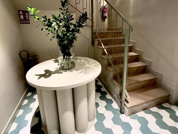 A staircase with a glass railing, a white round table with a plant, and a hexagonal patterned floor. - Ground Floor Apartment (Alicante)